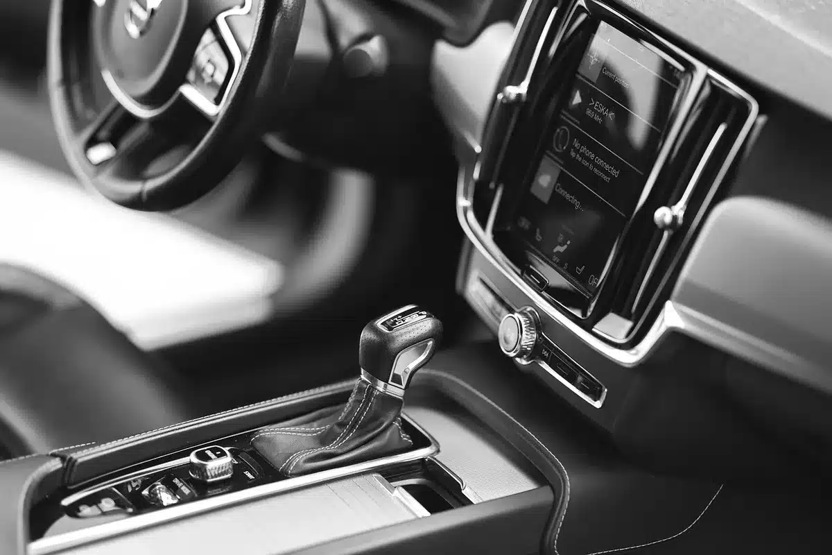 Hand holding smartphone near car infotainment showing app icons and settings