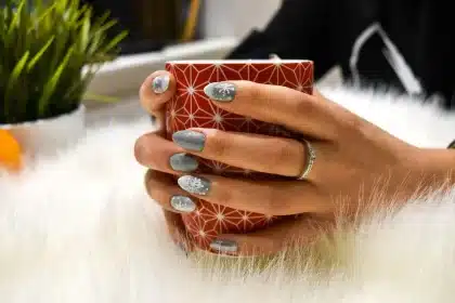 Close-up of hands with chocolate-brown glossy nail polish holding a warm mug in soft autumn lighting