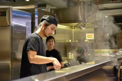 Hands of chefs plating dishes at two workstations in a busy restaurant kitchen