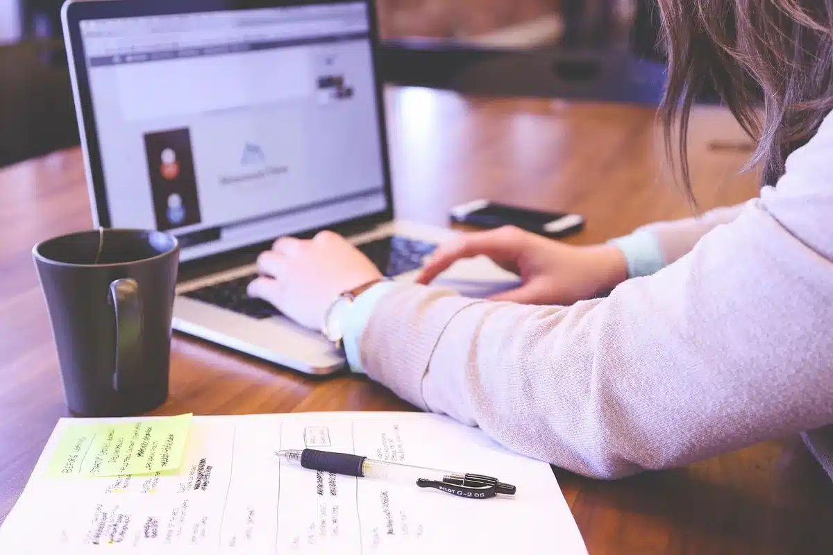 Hands typing on a laptop with a smartphone and notepad on a tidy desk