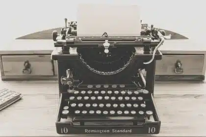Typewriter and loose manuscript pages on a rooftop at dusk, evoking a writer's solitude