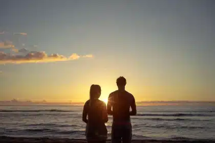 Silhouetted couple holding hands near a theater marquee with a stroller at dusk